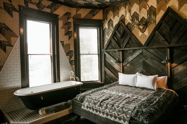 a bed in a room with multiple textures on the walls, including wooden herringbone slats, chevron panels, and subway tile