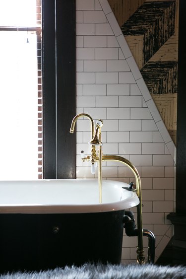 a porcelain tub with exposed brass taps next to a subway tile wall