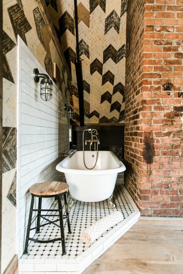 a clawfoot tub in a nook on a slightly raised tile platform in a bathroom with a herringbone tile ceiling