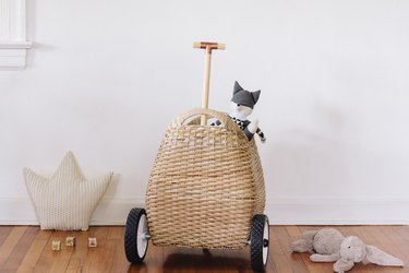 a wicker basket with a handle on wheels full of toys