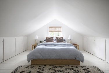a bed with a blue pinstripe comforter and two matching blonde-wood end tables under a steeply sloping roof