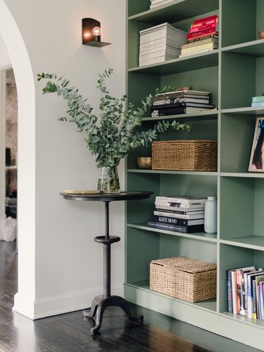 painted green built-in bookshelves styled with stacked booked and woven baskets