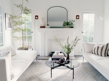 all white minimalist living room with two sofas facing each other, floor to ceiling windows, and a round glass coffee table