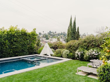 lawn next to backyard pool with pool loungers and lots of trees and greenery