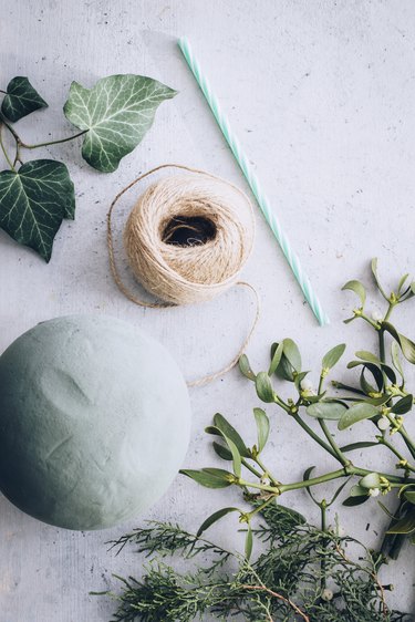 a foam floral ball, twine, a straw, mistletoe, and other greenery