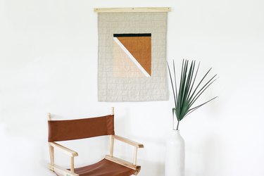 Painted quilt hanging with brown foldable chair and plant