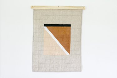White quilt with beige, brown, black pattern and wood beam