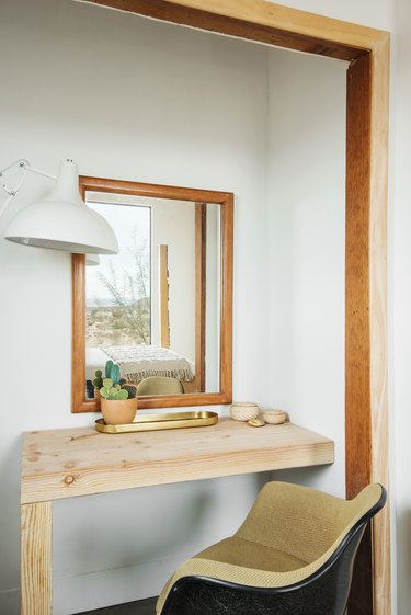 A wood desk with a plant and an office chair with a wood framed mirror