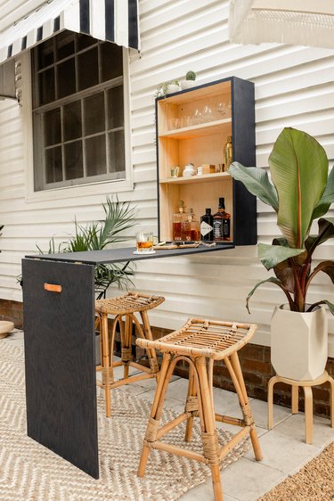 Patio with a black plywood bar table-cabinet set, tropical plants, lanterns, rattan furniture, and black-white accents
