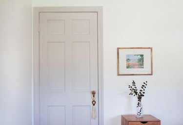 White door and white walls with framed art and side table to plant in vase