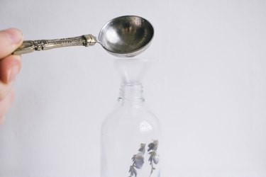 Spoon pouring liquid into a spray bottle with herbs through a funnel