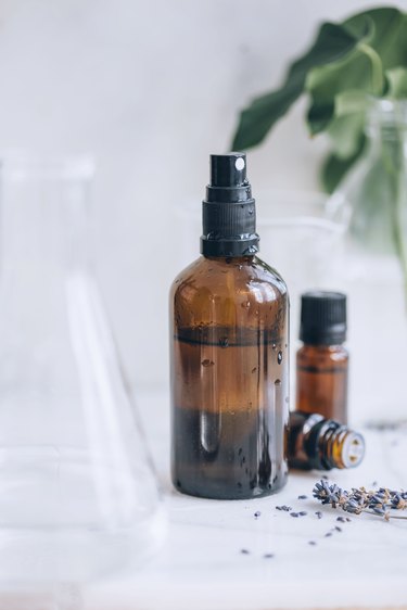 bottles of essential oil, lavender sprigs, a glass beaker, and a spray bottle full of diy room spray