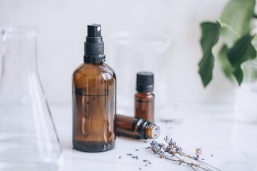bottles of essential oil, lavender sprigs, a glass beaker, and a spray bottle full of diy room spray