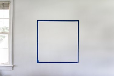 Blue painter's tape forming a square on a white wall next to window
