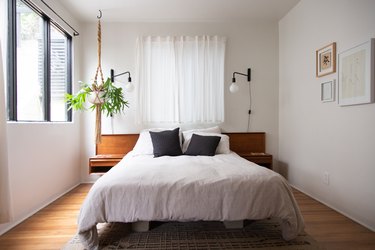 Minimalist bedroom with a wood headboard, macrame hanging planter, and globe wall lights.
