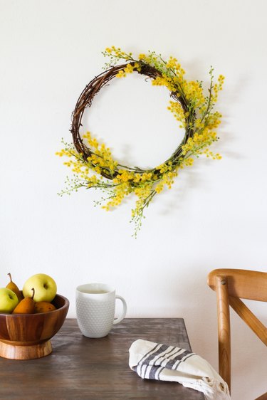 a wreath with tiny yellow flowers on a wall above a rustic wooden table
