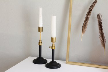 brass adjustable candlesticks next to a floating frame with feathers mounted in it