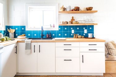 a kitchen with white cabinets, white walls, and a backsplash made of large azure tiles, each with a star in the center