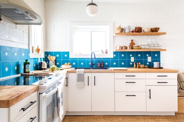 a kitchen with white cabinets, white walls, and a backsplash made of large azure tiles each with a star in the center