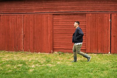 a man walks across green grass in front of a red barn