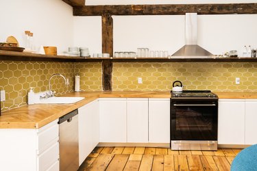 a kitchen with open shelving, wide-planked wooden floors, and a harvest-gold tile backsplash