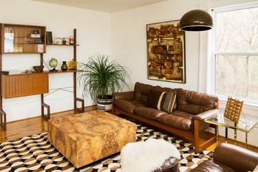 a brown leather couch and a marbled square coffee table in a room with brown abstract art and aa carpet with semi-circular patterns