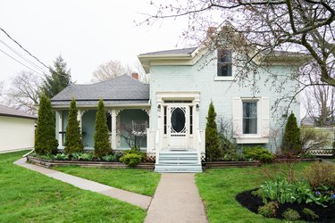 a sea-foam green two-story victorian house with a lush green lawn and a front door with a large glass pane