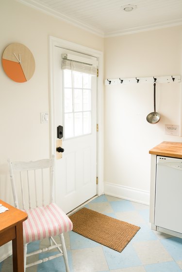a spare white kitchen with a numberless clock on the wall and a giant ladle hanging from a hook