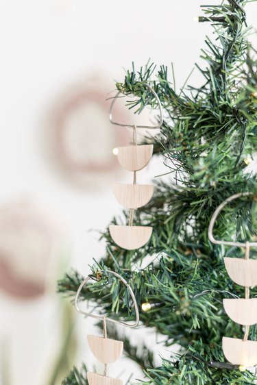 Scandi wood tree ornaments hanging off of small pine tree against white background