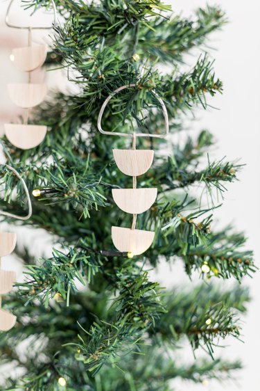 Scandi wood tree ornaments hanging off of small pine tree against white background