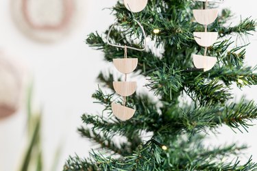 Scandi wood tree ornaments hanging off of small pine tree against white background