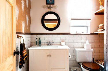 a bathroom with subway tile, a rustic wooden vanity and a cow-skull stencil patter on a wall