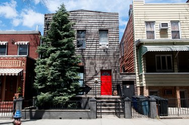 a two-story gray clapboard building with a bright red door