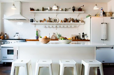 a kitchen with open shelving, a white refrigerator, white breakfast bar, and white metal stools