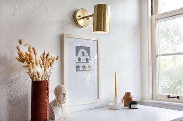 Wall sconce over art, vase with plant, sculpture, and candle
