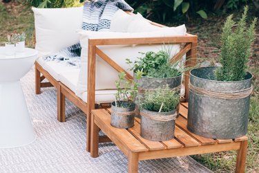 Wood side table with plants in metal planters next to white patio furniture
