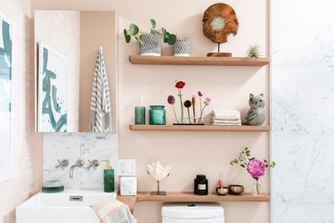 small boho bathroom with pink walls and wood shelving with flowers and plants