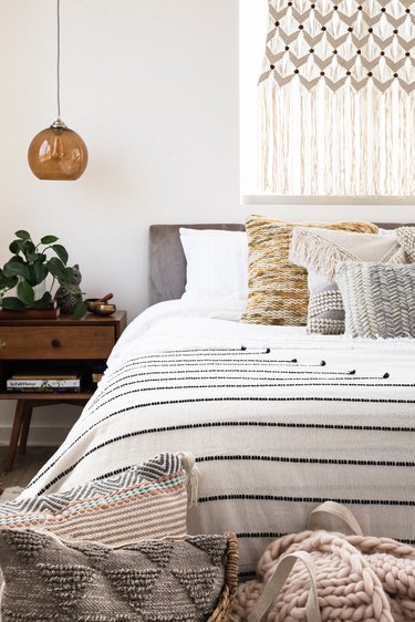 Bedroom with beige-neutral woven textile bedding and wall hanging