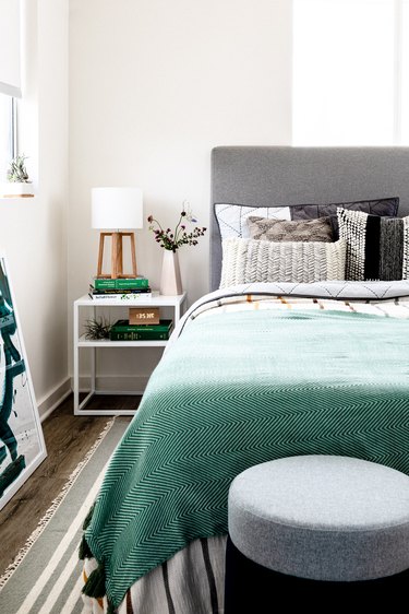 Bed with gray-turquoise bedding and pillows with nightstand and striped rug