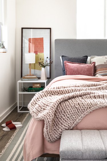 A bedroom with pink, gray, neutral bedding and furnishings