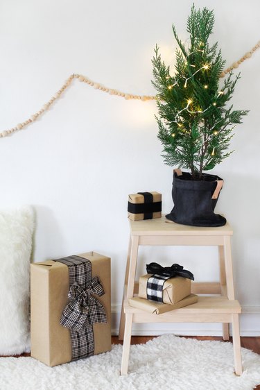 a small potted christmas tree decorated with a few lights sits on a stool