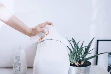 using a spray bottle to clean the arm of a couch