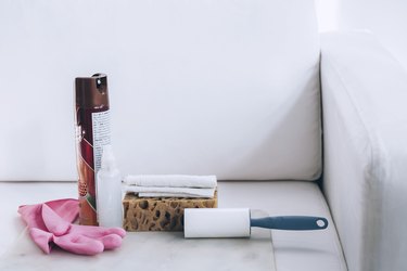 cleaning supplies including a lint roller, sponge, spray bottle, cloth, and furniture polish