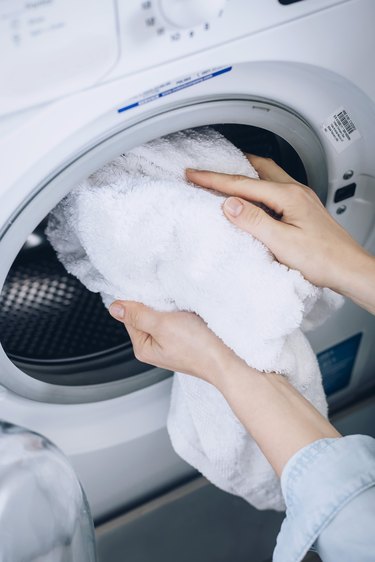Hand removing white towel from white clothing dryer