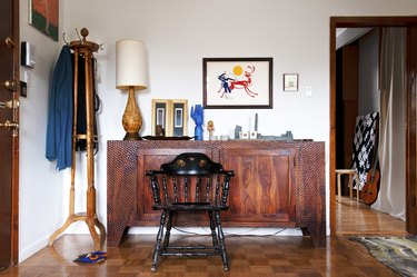 Wood credenza, sculptures, wood lamp, traditional art print, black spindle chair, coat rack, and wood checker floor.