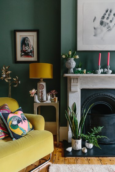 green walls and vintage marble fireplace next to a yellow velvet armchair