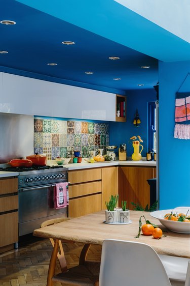 A kitchen with patchwork backsplash tiles, light wood bottom cabinets, and bright blue trim painted the same color as the walls.