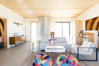 a woman relaxes in the mid-century living room with two colorful poufs in front of her