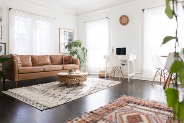 Bright living room with dark wood floor. An art wall, houseplant, brown leather sofa, a shag rug and a traditional rug.