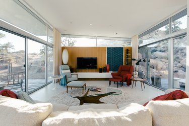 a light-flooded living room full of mid-century furniture, including a white shag rug, kidney-shaped coffee table, and a zeppelin-shaped pendant lamp